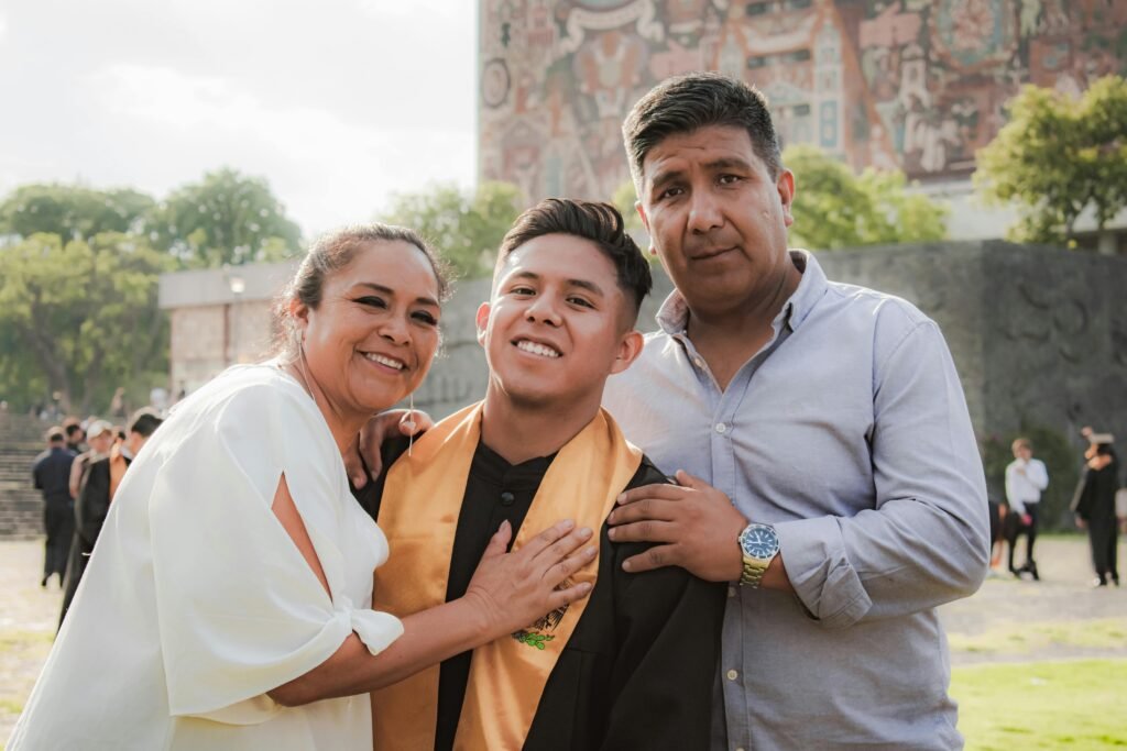 Family celebrates graduation with proud parents embracing their smiling graduate outdoors.